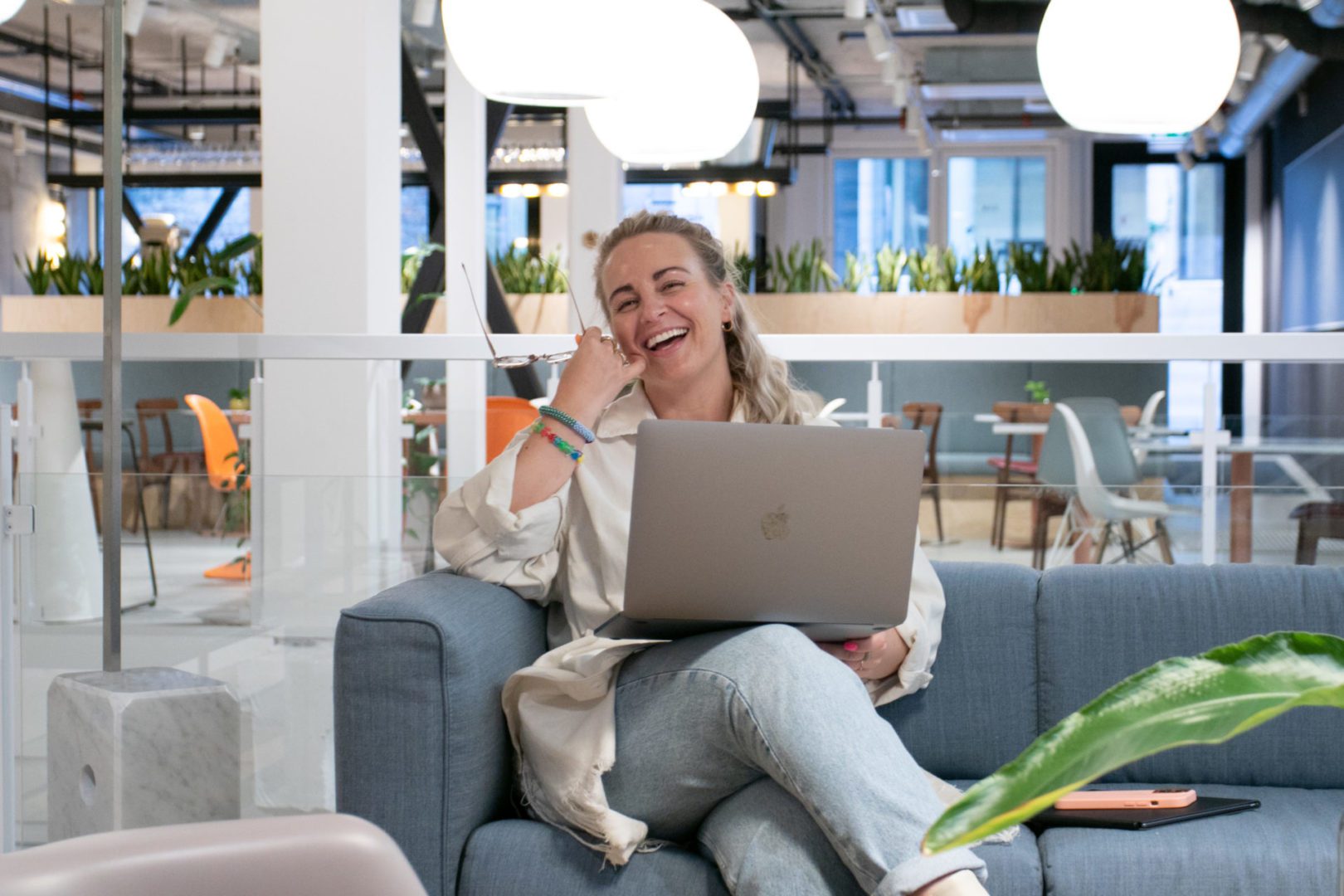 Markedssjefen Linn ler mens hun sitter i sofa og jobber på pc